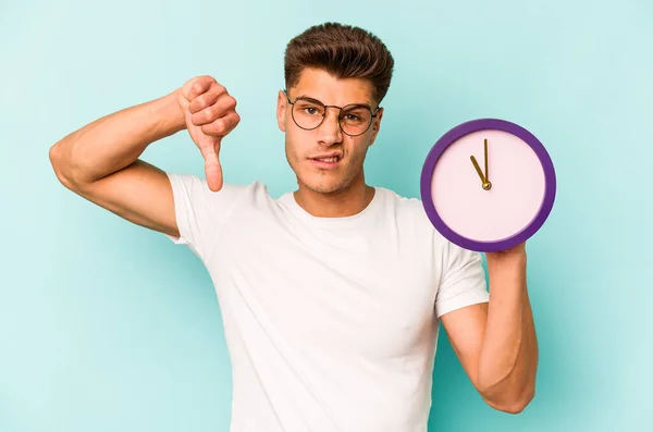 Young Caucasian Man Holding Clock Isolated Blue Background Showing Dislike — Stock Fotó