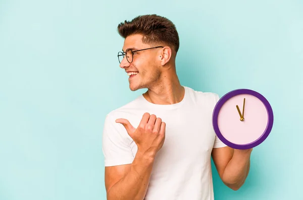 Young Caucasian Man Holding Clock Isolated Blue Background Points Thumb — ストック写真