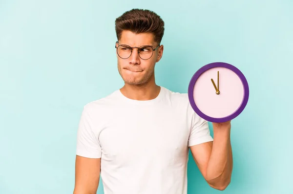 Young Caucasian Man Holding Clock Isolated Blue Background Confused Feels — Stock fotografie