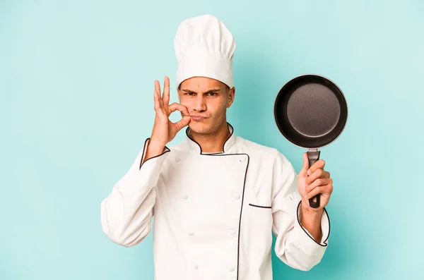 年轻的高加索厨师拿着用蓝色背景隔开的飞行锅 手指放在嘴唇上保守秘密 — 图库照片