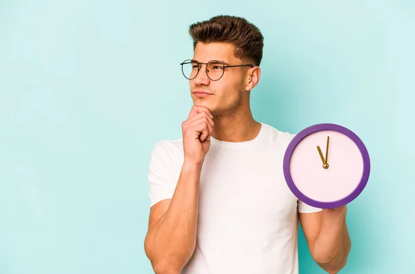 Young Caucasian Man Holding Clock Isolated Blue Background Looking Sideways — ストック写真