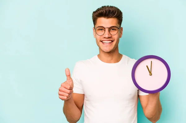 Young Caucasian Man Holding Clock Isolated Blue Background Smiling Raising — ストック写真