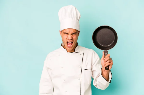 年轻的高加索厨师拿着一只被蓝色背景隔离的飞盘大喊大叫 非常愤怒和好斗 — 图库照片