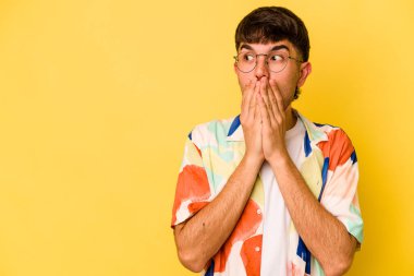 Kafkasyalı genç adam sarı arka planda izole edilmiş. Düşünceli bir şekilde, ağzını eliyle kapatan bir fotokopi odasına bakıyor..