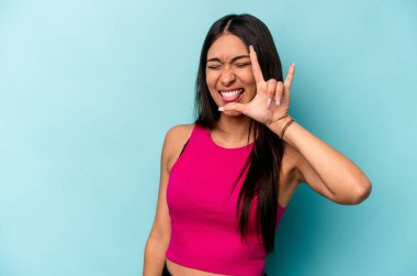 Mavi arka planda izole edilmiş genç İspanyol kadın parmaklarıyla taş hareketi gösteriyor.