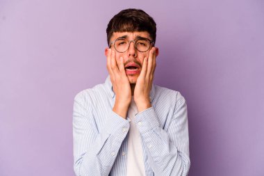 Mor arka planda izole edilmiş genç beyaz bir adam ağlıyor, bir şeyden memnun değil, acı ve kafa karışıklığı konsepti..
