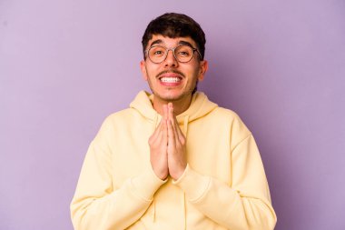 Mor arka planda izole olmuş genç beyaz bir adam el ele tutuşup, ağız kenarında dua ediyor, kendinden emin..