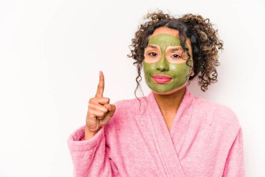 Yüz maskesi takan genç İspanyol kadın beyaz arka planda bir numarayı parmağıyla gösteriyor..