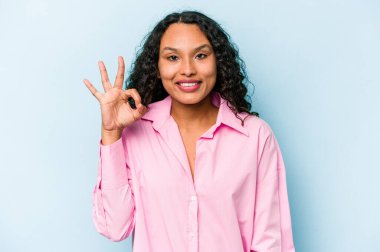 Genç İspanyol kadın mavi arka planda izole edilmiş neşeli ve kendinden emin, iyi bir hareket gösteriyor..