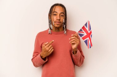 Beyaz arka planda izole edilmiş İngiliz bayrağı tutan genç bir Afro-Amerikan erkeği sanki sizi davet ediyormuş gibi parmağıyla işaret ediyor..