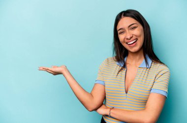 Mavi arka planda izole edilmiş genç İspanyol kadın bir avuç içinde fotokopi alanı ve belinde bir el daha gösteriyor..