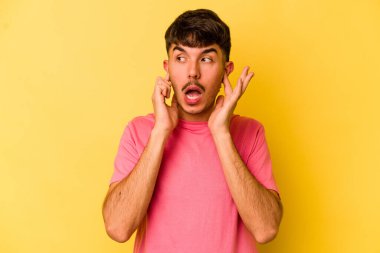Sarı arka planda izole edilmiş genç beyaz bir adam parmaklarıyla kulaklarını kapatıyor, gürültülü bir ortam yüzünden stresli ve çaresiz..