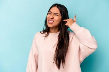 Mavi arka planda izole edilmiş genç İspanyol kadın kulaklarını elleriyle kapatıyor..