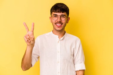 Sarı arka planda izole edilmiş genç beyaz adam neşeli ve kaygısız parmakları olan bir barış sembolü gösteriyor..