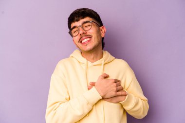 Mor arka planda izole edilmiş beyaz bir genç, dost bir ifadeye sahip, avuçlarını göğsüne bastırıyor. Aşk konsepti.