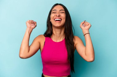 Mavi arka planda izole edilmiş genç İspanyol kadın zaferi, tutkuyu ve coşkuyu, mutlu ifadeyi kutluyor..