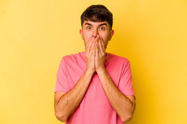 Sarı arka planda izole edilmiş genç beyaz adam şok olmuş, ağzı ellerle kaplanmış, yeni bir şey keşfetmeye hevesli..