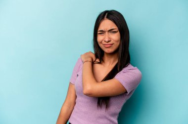 Mavi arka planda izole edilmiş genç İspanyol kadın omuz ağrısı çekiyor..