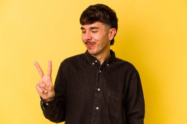 Sarı arka planda izole edilmiş genç beyaz adam neşeli ve kaygısız parmakları olan bir barış sembolü gösteriyor..