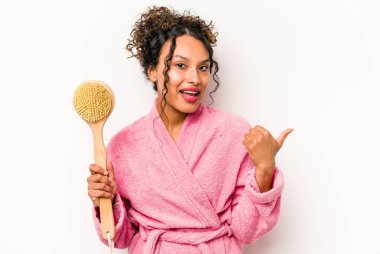 Sırt kaşıyıcı tutan genç İspanyol kadın beyaz arka planda izole edilmiş, baş parmak uzakta, gülen ve kaygısız..