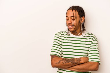 Beyaz arka planda izole edilmiş genç Afro-Amerikalı adam kollarını kavuşturarak gülümsüyor..