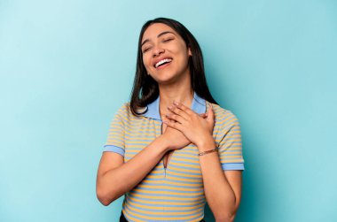 Mavi arka planda izole edilmiş genç İspanyol kadın avuçlarını göğsüne bastıran dostça bir ifadeye sahiptir. Aşk konsepti.