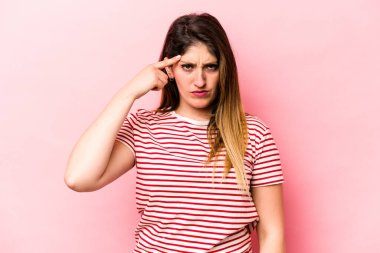 Pembe arka planda izole edilmiş beyaz bir kadın şakağı parmağıyla işaret ediyor, düşünüyor ve bir göreve odaklanıyor..