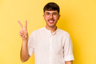 Sarı arka planda izole edilmiş genç beyaz adam iki numarayı parmaklarıyla gösteriyor..