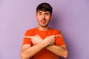 Mor arka plan noktalarında izole genç beyaz adam, iki seçenek arasında seçim yapmaya çalışıyor.