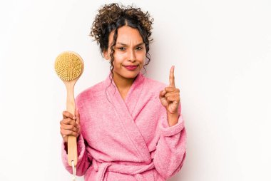 Sırt kaşıyıcısı tutan genç İspanyol kadın beyaz arka planda bir numarayı parmağıyla gösteriyor..