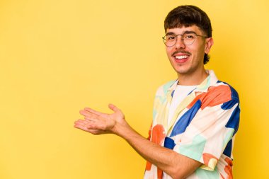 Sarı arka planda izole edilmiş genç beyaz bir adam palmiyesinde bir kopya alanı tutuyor..