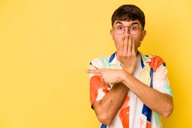 Sarı arka planda izole edilmiş genç beyaz adam yan tarafı işaret ediyor.