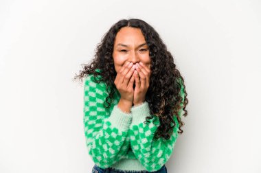 Beyaz arka planda izole edilmiş genç İspanyol kadın bir şeye gülüyor, elleriyle ağzını kapatıyor..