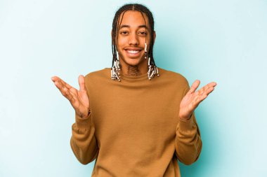 Genç Afrikalı Amerikalı bir adam mavi arka planda izole edilmiş. Hoş bir sürpriz, heyecanlı ve el kaldırıyor..