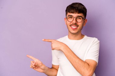 Mor arka planda izole edilmiş genç beyaz adam işaret parmağıyla işaret ederek heyecanlanıyor..