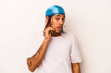 Genç Afrikalı Amerikalı adam beyaz arka planda izole edilmiş bir şekilde bir dedikoduyu dinlemeye çalışıyor..