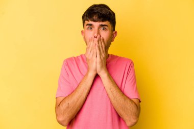 Sarı arka planda izole edilmiş genç beyaz adam elleri endişeli bir şekilde ağzı örtüyor..