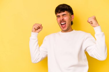 Sarı arka planda izole edilmiş genç beyaz adam zaferden sonra yumruğunu kaldırıyor, kazanan konsept..