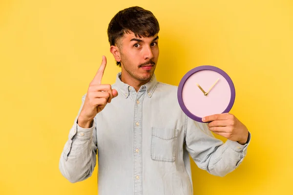 Молодий Іспаномовний Чоловік Тримає Годинник Ізольований Жовтому Тлі Показуючи Номер — стокове фото