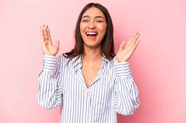 Genç İspanyol kadın pembe arka planda izole edilmiş. Hoş bir sürpriz bekliyor. Heyecanlı ve el kaldırıyor..