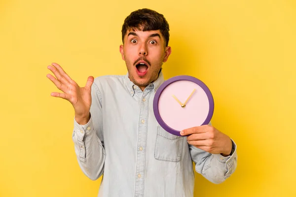 Joven Hispano Sosteniendo Reloj Aislado Sobre Fondo Amarillo Sorprendido Sorprendido — Foto de Stock