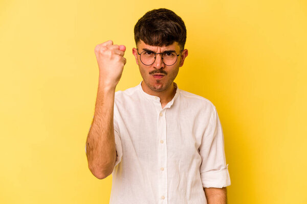Young caucasian man isolated on yellow background showing fist to camera, aggressive facial expression.