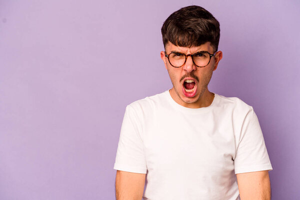 Young caucasian man isolated on purple background shouting very angry, rage concept, frustrated.
