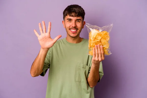 Jonge Spaanse Man Met Chips Geïsoleerd Paarse Achtergrond Lachend Vrolijk — Stockfoto