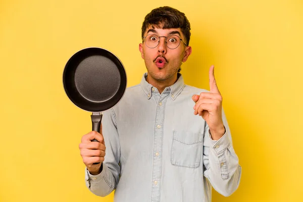 黄色の背景に孤立したフライパンを保持する若いヒスパニック炊飯器いくつかの素晴らしいアイデア 創造性の概念 — ストック写真