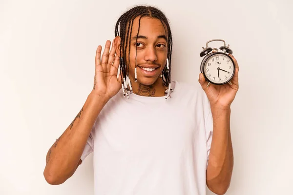 Jovem Afro Americano Segurando Despertador Isolado Fundo Branco Tentando Ouvir — Fotografia de Stock