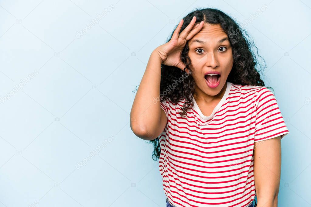 Young hispanic woman isolated on blue background shouts loud, keeps eyes opened and hands tense.
