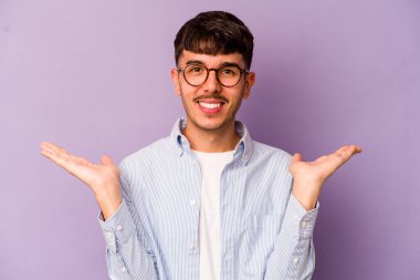 Mor arka planda izole genç beyaz adam kollarıyla ölçek yapar, mutlu ve kendinden emin hisseder..