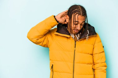 Genç Afrikalı Amerikalı adam mavi arka planda izole edilmiş kafasının arkasına dokunuyor, düşünüyor ve bir seçim yapıyor..