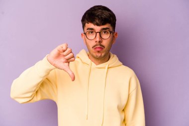 Mor arka planda izole edilmiş genç beyaz bir adam hoş olmayan bir jest yapıyor, başparmakları aşağıda. Anlaşmazlık konsepti.